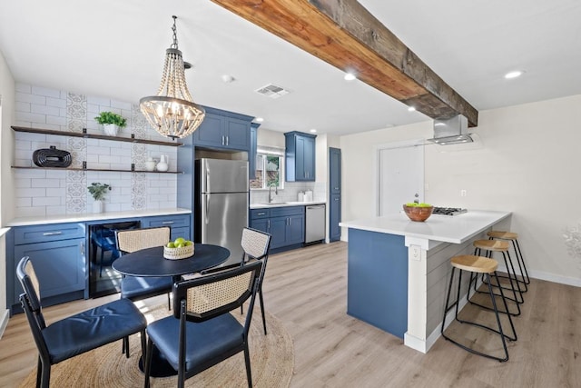 kitchen featuring light wood finished floors, a kitchen breakfast bar, a peninsula, stainless steel appliances, and blue cabinets