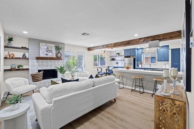 living area with visible vents, recessed lighting, beamed ceiling, light wood-type flooring, and a large fireplace