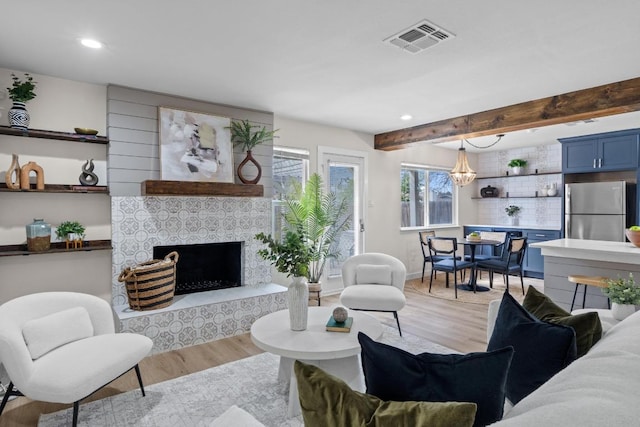 living area with visible vents, light wood finished floors, beam ceiling, and a tile fireplace