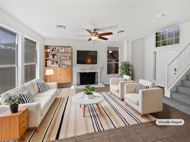 living area featuring tile patterned flooring, visible vents, a fireplace with raised hearth, and stairs