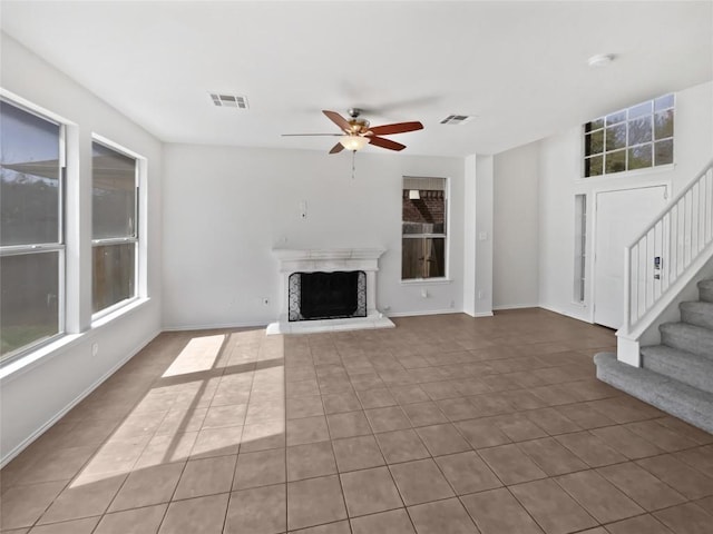 unfurnished living room with visible vents, a fireplace with raised hearth, a ceiling fan, and stairway