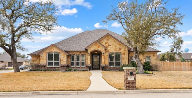 french country style house featuring a front lawn, fence, brick siding, and a shingled roof