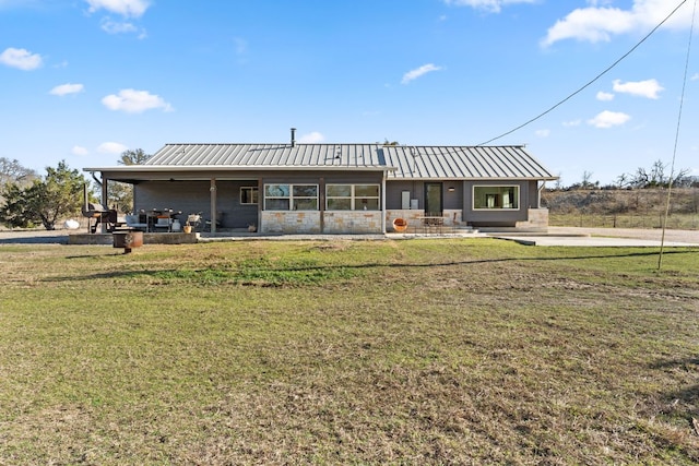 view of front of home featuring a front lawn, a standing seam roof, stone siding, metal roof, and a patio area