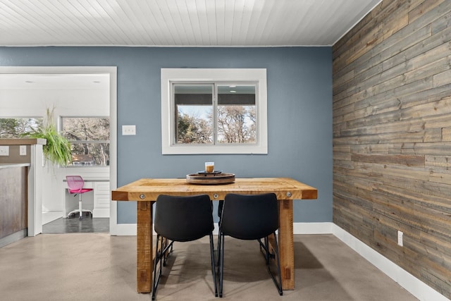 dining space with wood walls, concrete floors, and baseboards