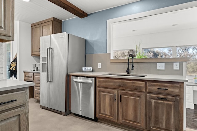 kitchen featuring beamed ceiling, stainless steel appliances, light countertops, and a sink