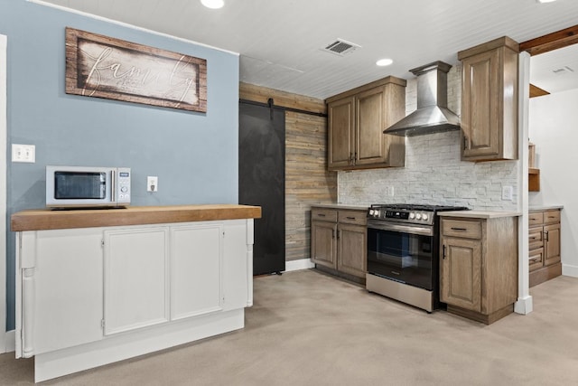 kitchen with visible vents, concrete floors, appliances with stainless steel finishes, a barn door, and wall chimney range hood