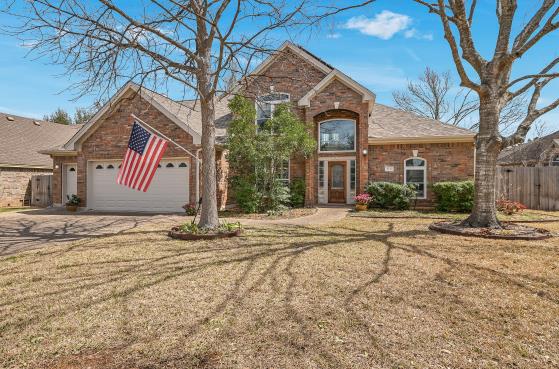 traditional-style home with brick siding, a front lawn, fence, driveway, and an attached garage