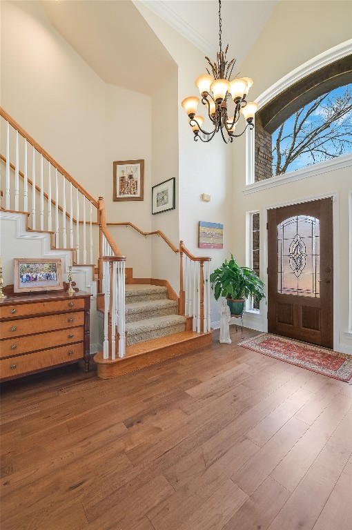 foyer with stairway, wood finished floors, high vaulted ceiling, crown molding, and a notable chandelier