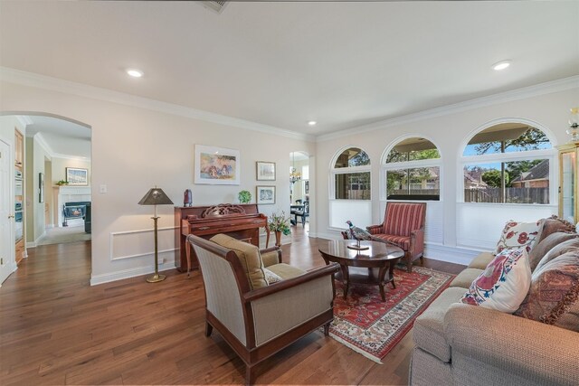 living room with ornamental molding, a glass covered fireplace, wood finished floors, arched walkways, and baseboards