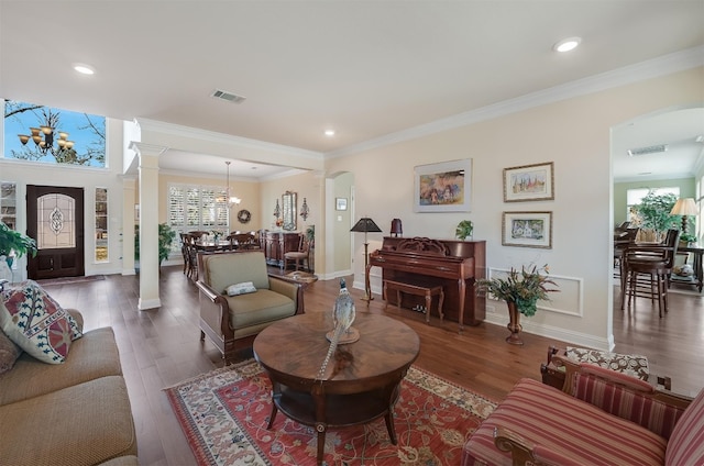 living area featuring arched walkways, visible vents, wood finished floors, and decorative columns