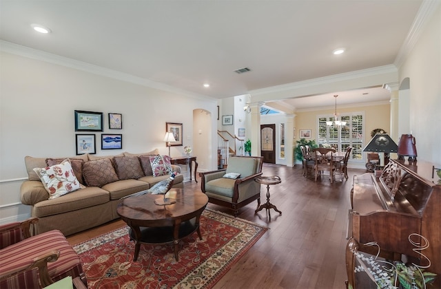 living room featuring stairway, visible vents, dark wood finished floors, decorative columns, and crown molding