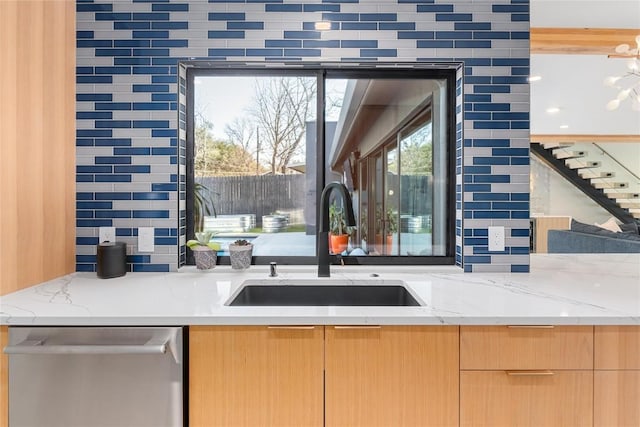 kitchen with light stone countertops, light brown cabinetry, a sink, stainless steel dishwasher, and backsplash