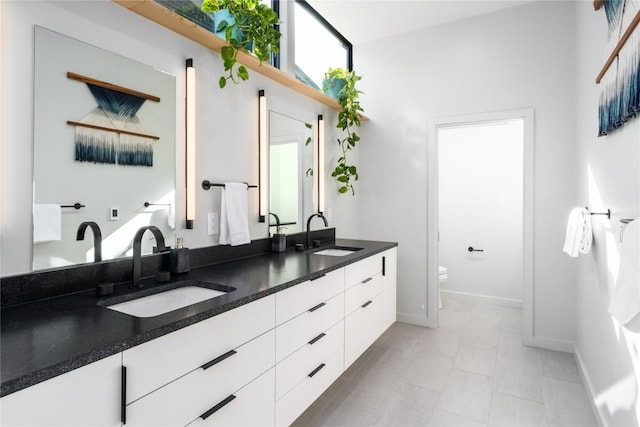 bathroom featuring double vanity, toilet, baseboards, and a sink