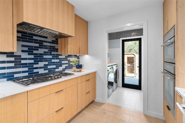 kitchen featuring washing machine and clothes dryer, light brown cabinetry, decorative backsplash, appliances with stainless steel finishes, and modern cabinets