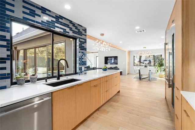 kitchen featuring light brown cabinetry, stainless steel dishwasher, an inviting chandelier, modern cabinets, and a sink