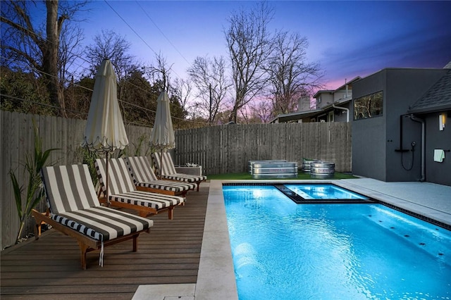 pool at dusk with a deck, a fenced in pool, an in ground hot tub, and a fenced backyard