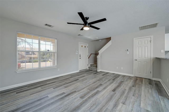 unfurnished living room with stairs, wood finished floors, visible vents, and baseboards