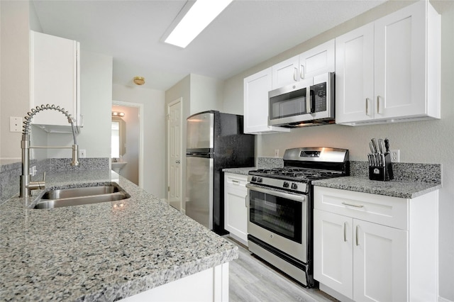 kitchen featuring light wood-type flooring, light stone counters, stainless steel appliances, white cabinetry, and a sink