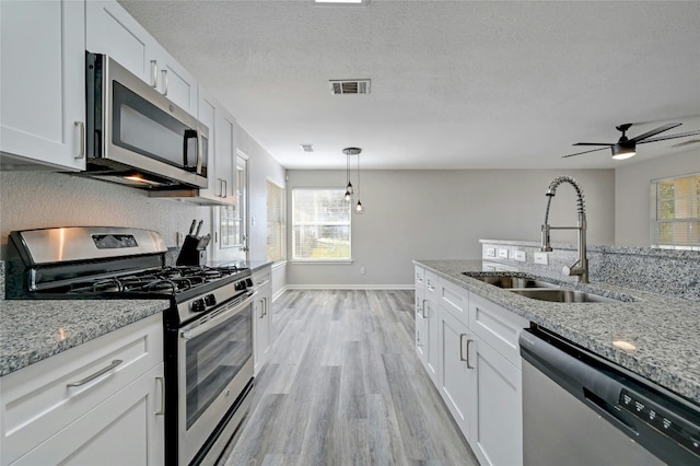 kitchen featuring a sink, stainless steel appliances, white cabinets, a textured ceiling, and light wood-type flooring