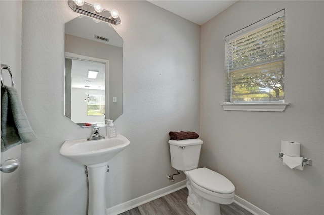 half bathroom with visible vents, toilet, wood finished floors, and baseboards