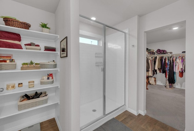 full bath with a walk in closet, a stall shower, wood finished floors, recessed lighting, and baseboards