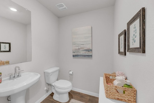 half bath with wood finished floors, baseboards, visible vents, a sink, and toilet