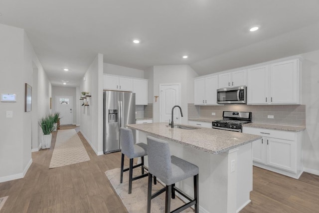 kitchen with a sink, appliances with stainless steel finishes, a kitchen island with sink, and light wood finished floors