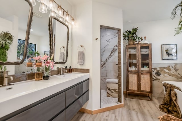 bathroom with double vanity, wood finished floors, a tile shower, and a sink