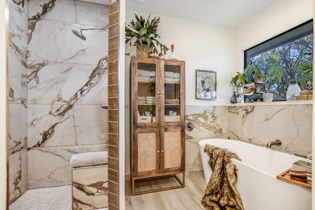 full bath with a soaking tub, tile walls, wood finished floors, and a tile shower