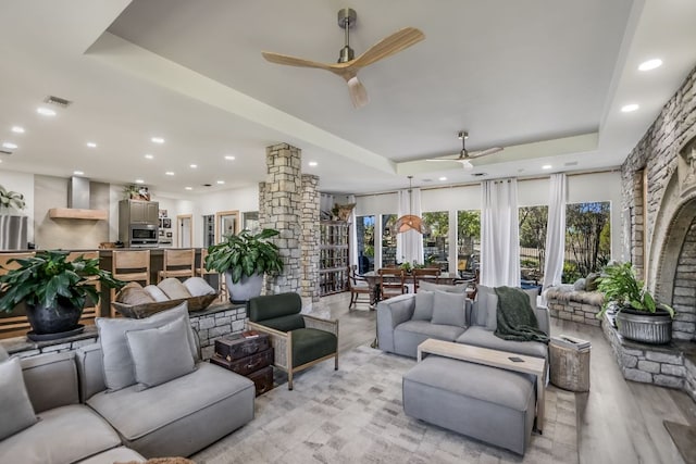 living area with visible vents, ceiling fan, decorative columns, light wood-style floors, and a raised ceiling