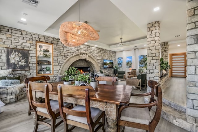 dining space featuring visible vents, a tray ceiling, decorative columns, a warm lit fireplace, and wood finished floors