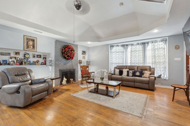 living area with visible vents, a brick fireplace, a raised ceiling, and wood-type flooring