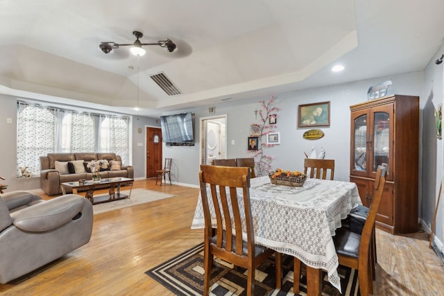 dining area with visible vents, a raised ceiling, light wood-type flooring, and vaulted ceiling