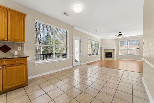 unfurnished living room with visible vents, a fireplace, light tile patterned floors, baseboards, and ceiling fan