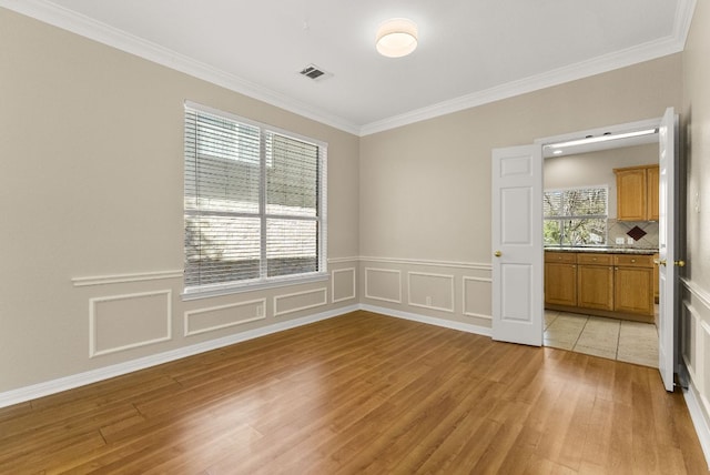 spare room with visible vents, light wood finished floors, ornamental molding, wainscoting, and a decorative wall