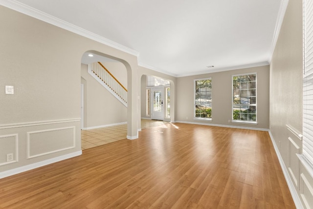 unfurnished living room with stairway, arched walkways, light wood-style flooring, and crown molding