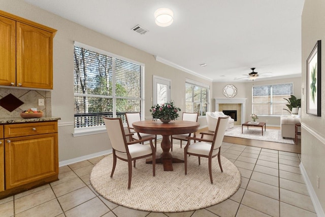 dining space with crown molding, light tile patterned flooring, visible vents, and a tile fireplace