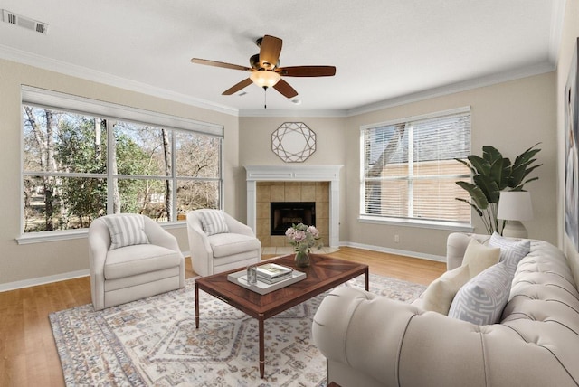 living area with wood finished floors, baseboards, visible vents, a tile fireplace, and crown molding