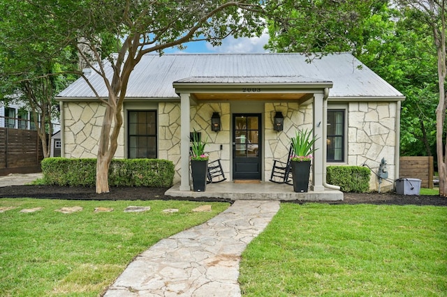 view of front of house with a front lawn, covered porch, stone siding, and metal roof