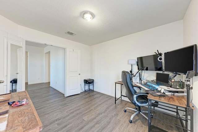 office area with baseboards, wood finished floors, visible vents, and a textured ceiling