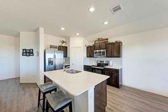 kitchen featuring a center island with sink, visible vents, a sink, stainless steel appliances, and dark brown cabinets