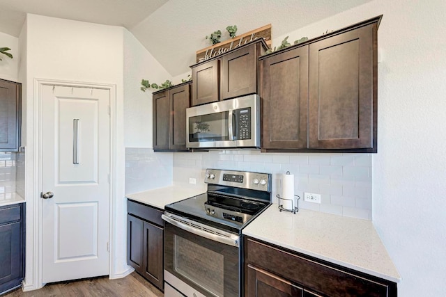 kitchen with wood finished floors, lofted ceiling, dark brown cabinets, appliances with stainless steel finishes, and backsplash