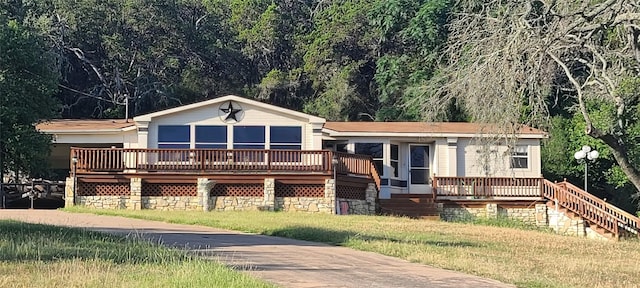 view of front of property featuring a wooden deck, a front lawn, and a view of trees