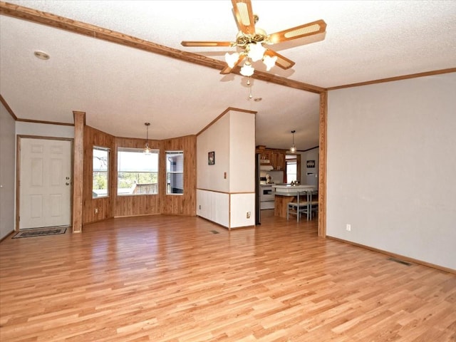 unfurnished living room with crown molding, light wood-style floors, wood walls, and a textured ceiling