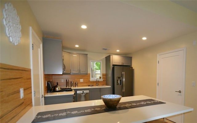 kitchen featuring backsplash, light countertops, gray cabinets, appliances with stainless steel finishes, and a sink