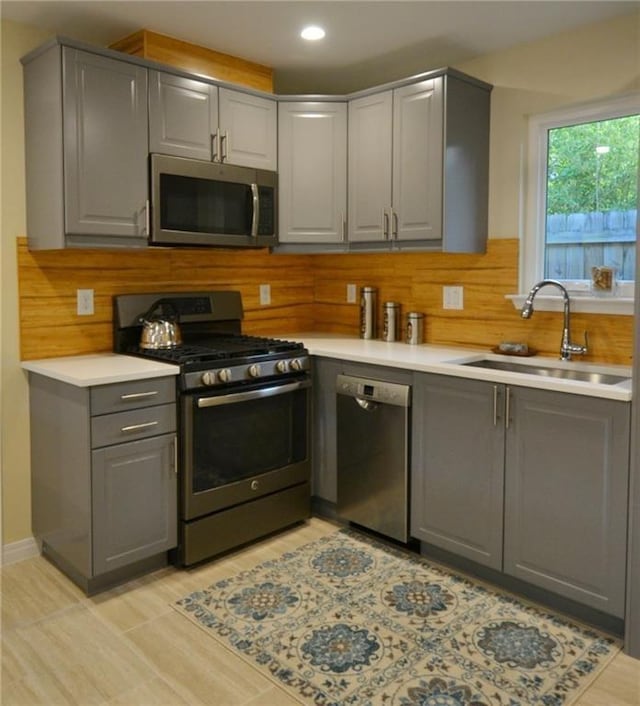 kitchen with gray cabinets, a sink, tasteful backsplash, stainless steel appliances, and light countertops