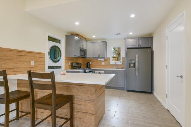 1705 E 14th St Unit B, Austin, TX 78702 - kitchen with appliances with stainless steel finishes, gray cabinetry, stacked washer / drying machine, light countertops, and tasteful backsplash