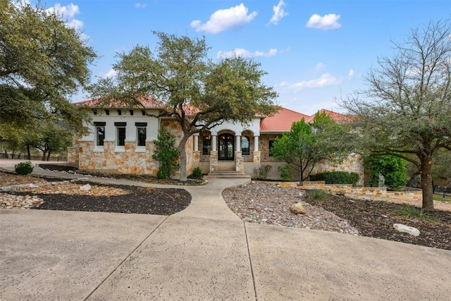 mediterranean / spanish-style home with stone siding, stucco siding, french doors, and a tile roof