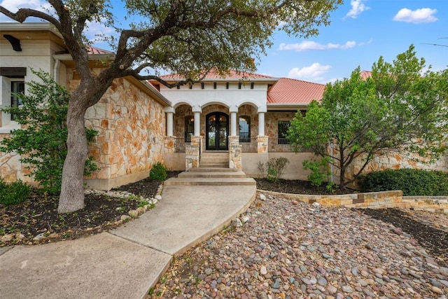 mediterranean / spanish-style house with french doors, stone siding, stucco siding, and a tile roof