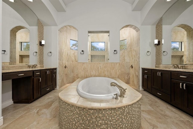 full bath featuring vaulted ceiling, two vanities, a garden tub, and a sink